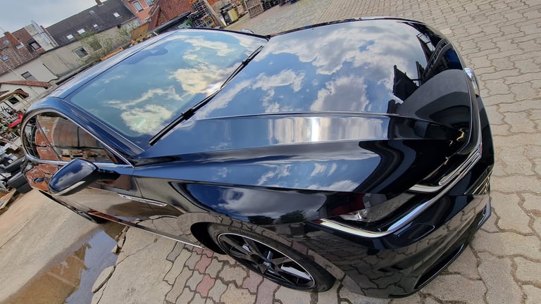 Black sedan parked on brick pavement with open driver door, reflecting sky and clouds