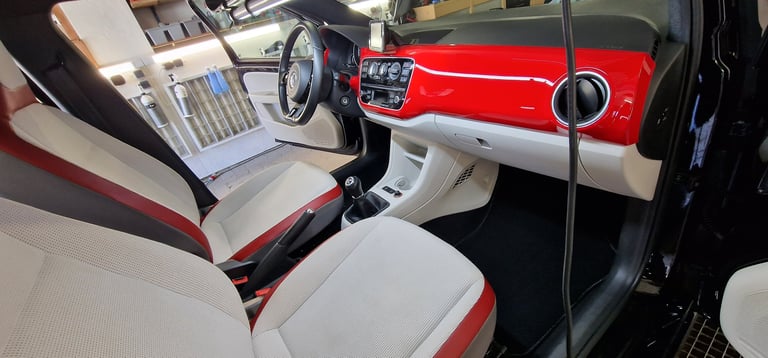 Interior of a classic red and white car showing steering wheel, dashboard, and beige and red upholstered seats