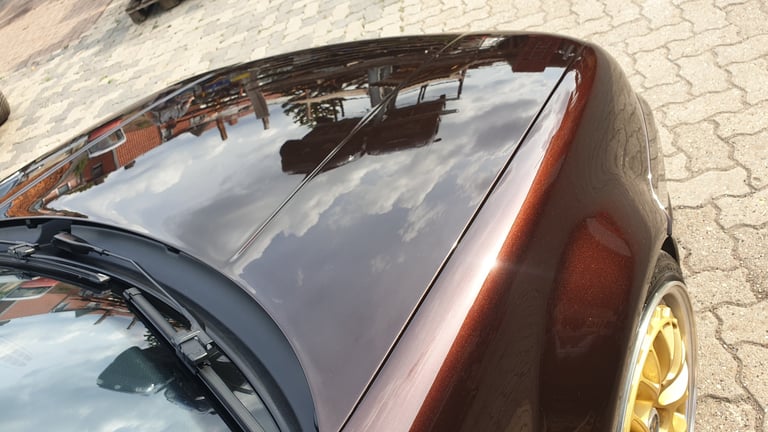 Close-up of a damaged car roof and rear window with rust and deterioration, viewed from above on a textured surface