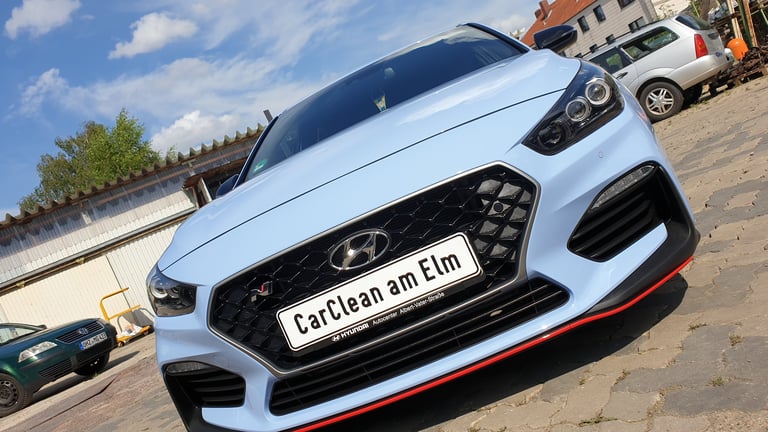 White sports car with CarClean am Elm license plate at outdoor car wash facility