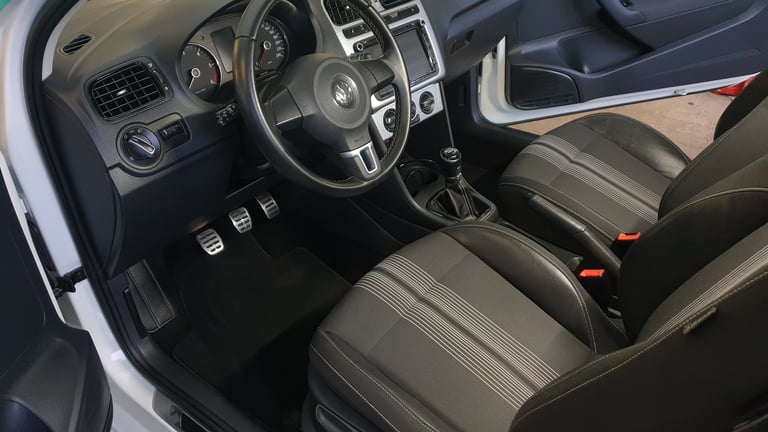 Interior view of a sports car with black leather steering wheel, gray striped seats, and modern dashboard with digital controls