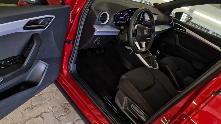 Interior view of a red car with black leather seats, steering wheel, dashboard, and open driver side door