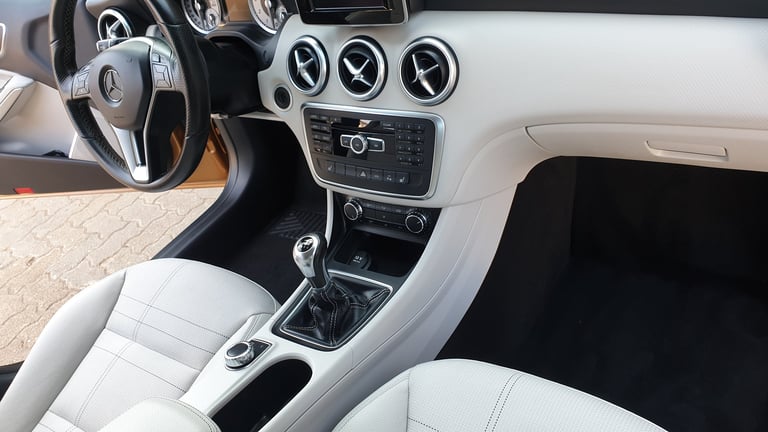 Interior view of a car showing white leather seats, steering wheel, dashboard with gauges, and manual transmission shifter