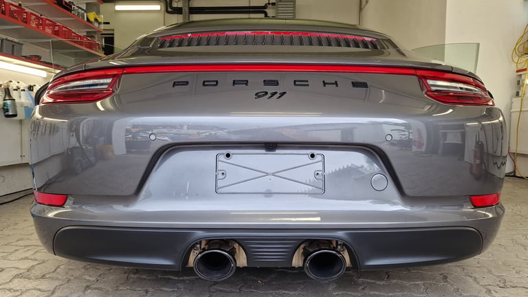 Rear view of a red and gray Porsche 911 with dual exhaust pipes in a garage setting