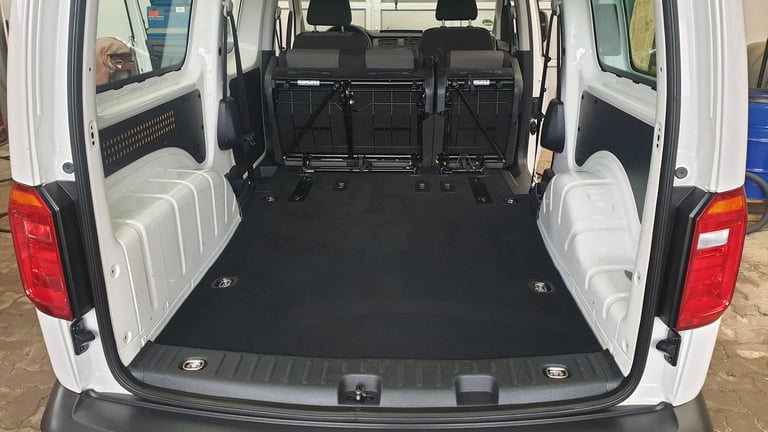 Interior view of white cargo van with open rear doors, showing black rubber floor mat and white passenger seats on sides